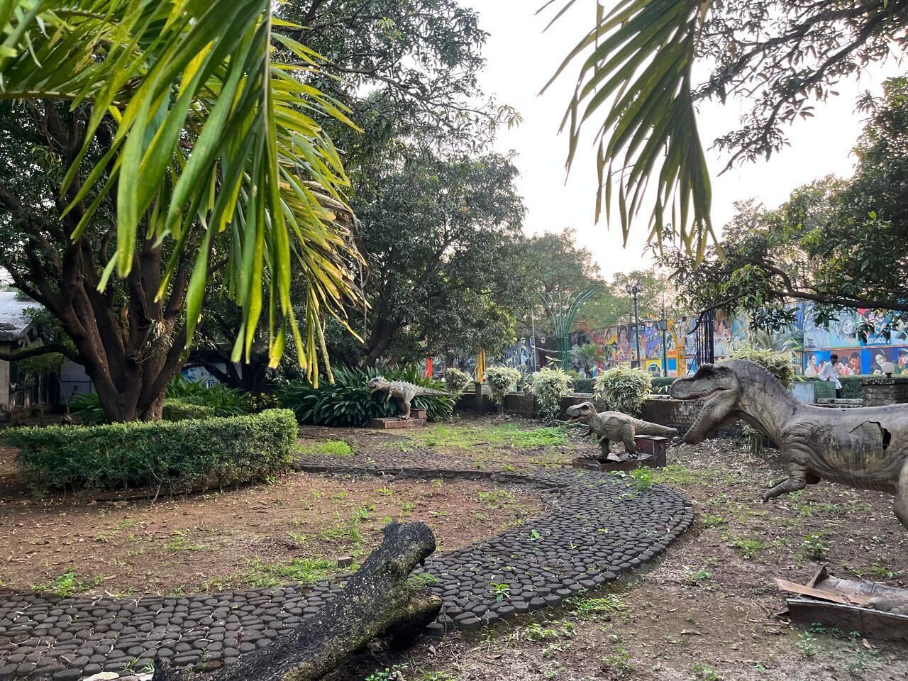 Eine Dinosaurierausstellung mit lebensgroßen Modellen, umgeben von üppigem Grün und einem gepflasterten Weg.