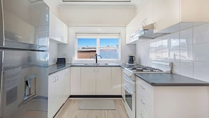 A modern kitchen with stainless steel appliances, white cabinetry, and a window providing a view. - Metawisebnb Cozy 2bed Earlwood Near City Airport (Sydney)