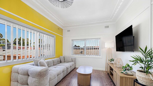 A modern living room with a sectional sofa, a round coffee table, and a wooden console table with decorative items. - Metawisebnb Cozy 2bed Earlwood Near City Airport (Sydney)