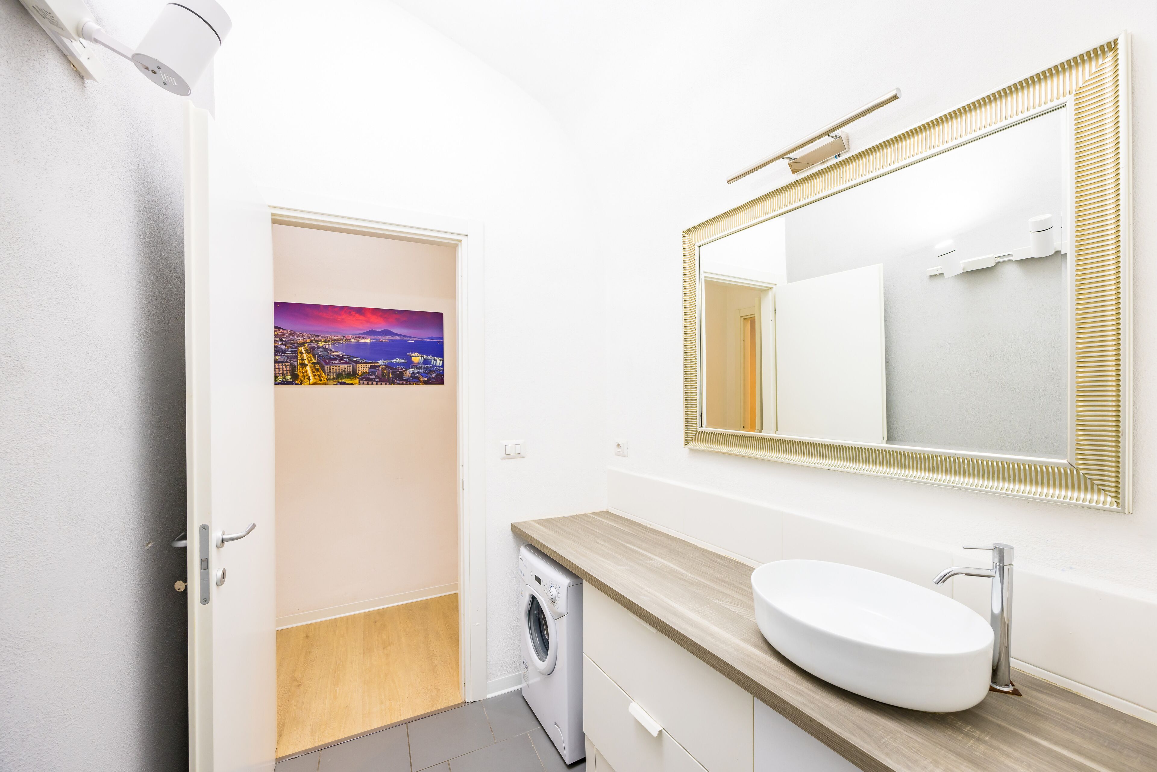 A modern bathroom with a built-in washing machine, a large mirror with a gold frame, and a wooden vanity.