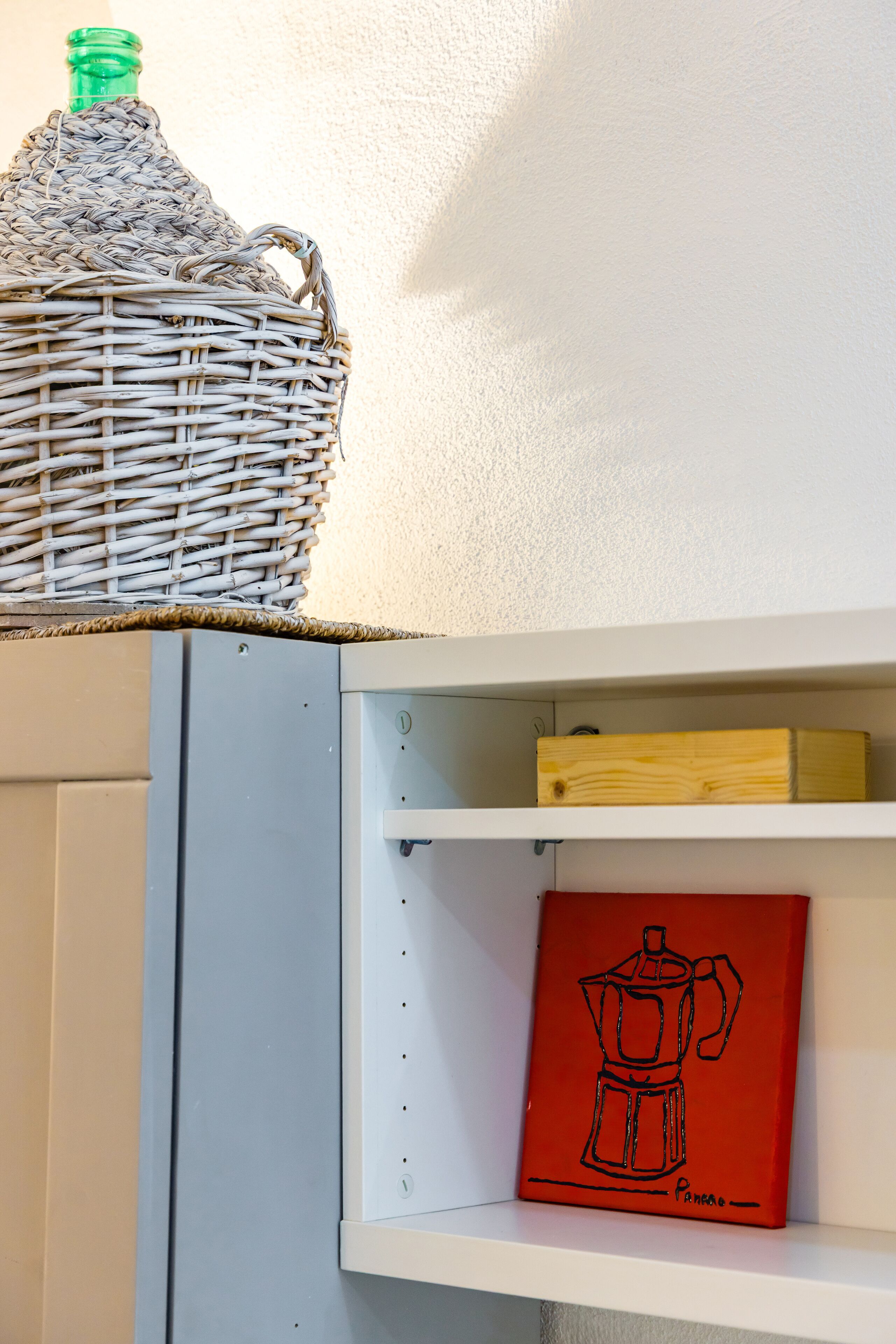 A wicker basket on a shelf, a wooden box, and a red artwork of a coffee pot.