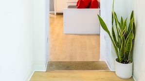A hallway leading to a room with a white cabinet, a red pillow on a white sofa, and a potted plant. - O Panaro Lucky Flat by NapoliApartments (Naples)