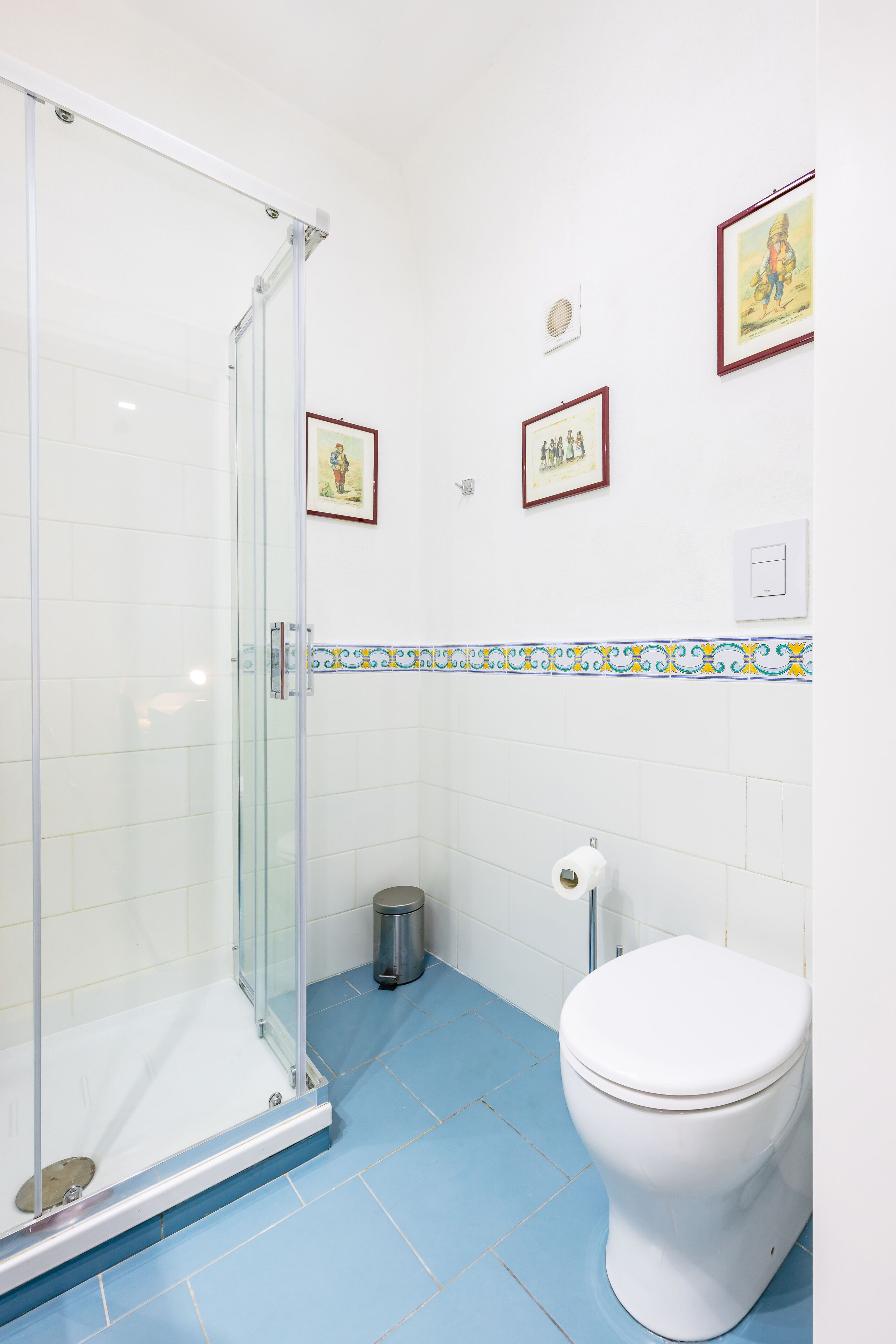 A bathroom with a glass shower enclosure, a toilet, and decorative tiles.