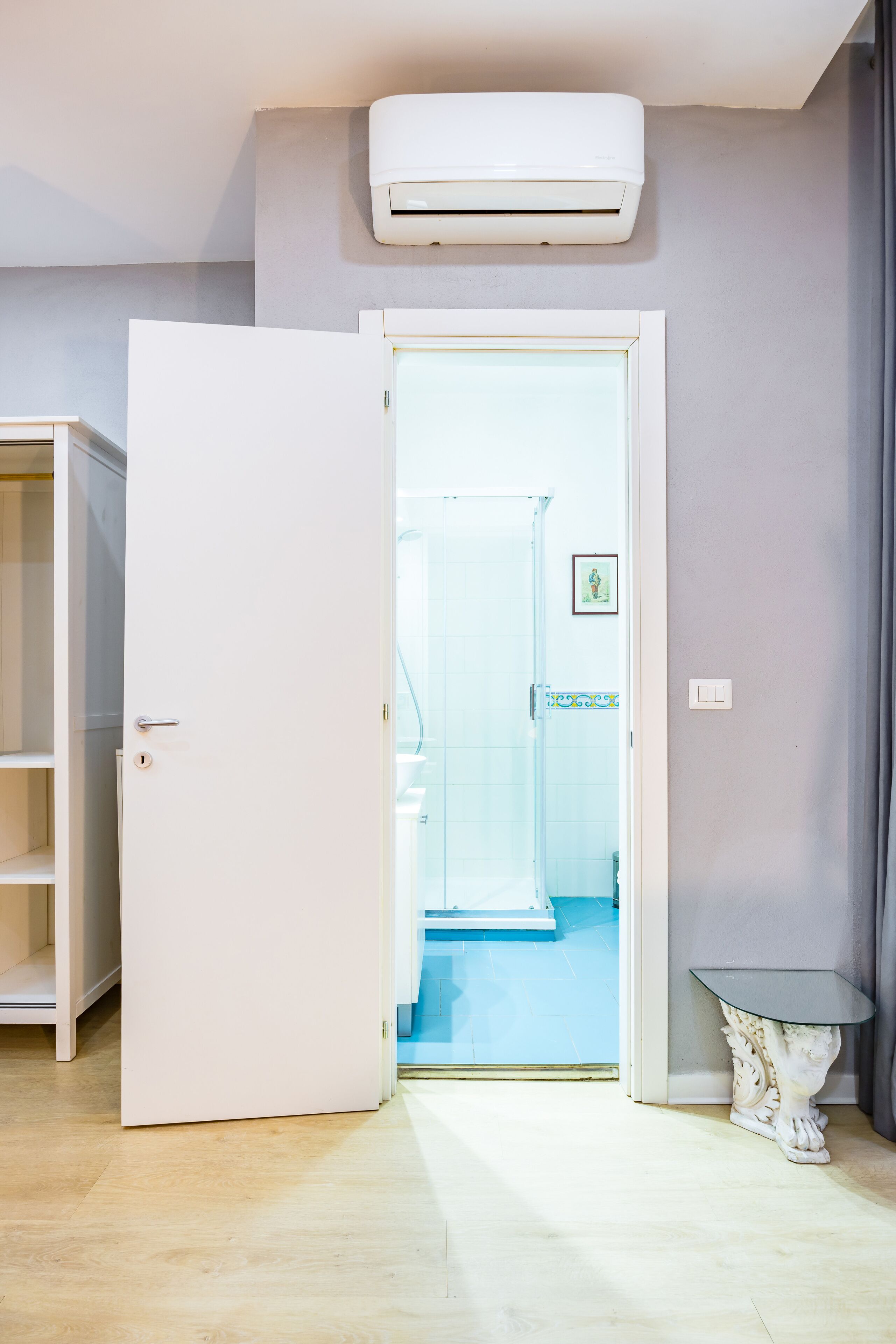 A room with a white door, a white air conditioner, a small white table, and a blue tiled floor.