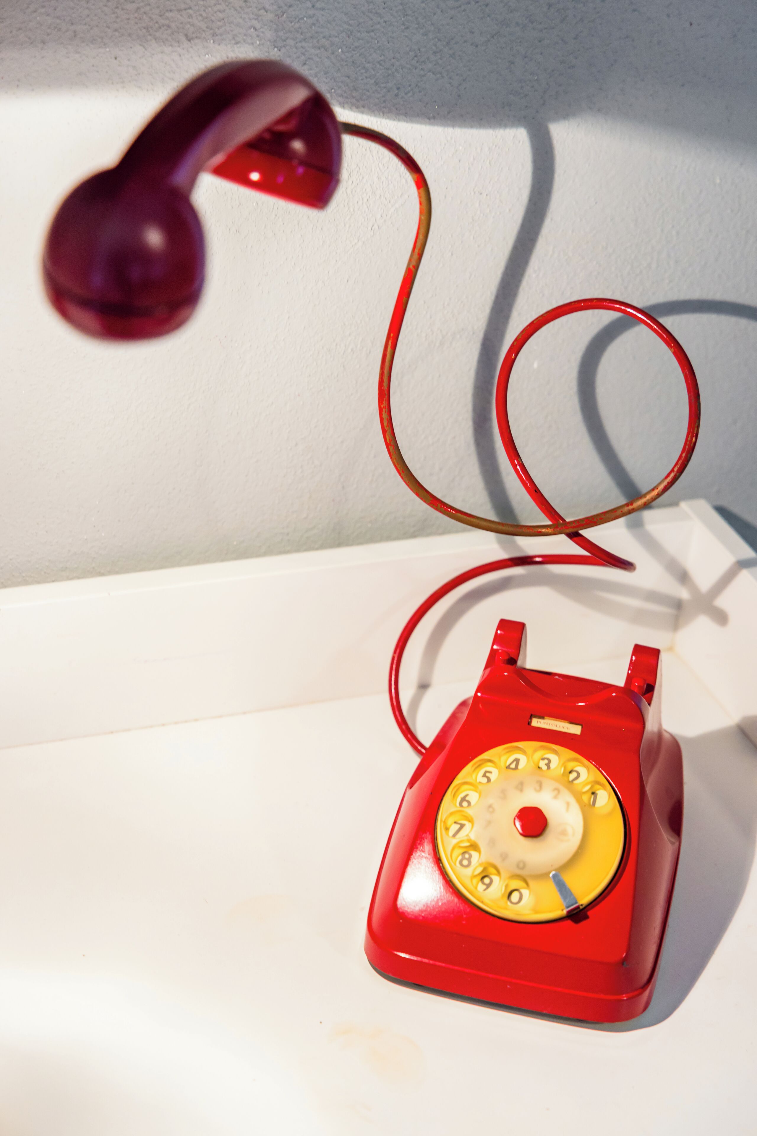 A red rotary telephone on a white surface.
