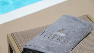 Una toalla doblada con el bordado 'LITHOS', sobre una silla junto a una piscina.