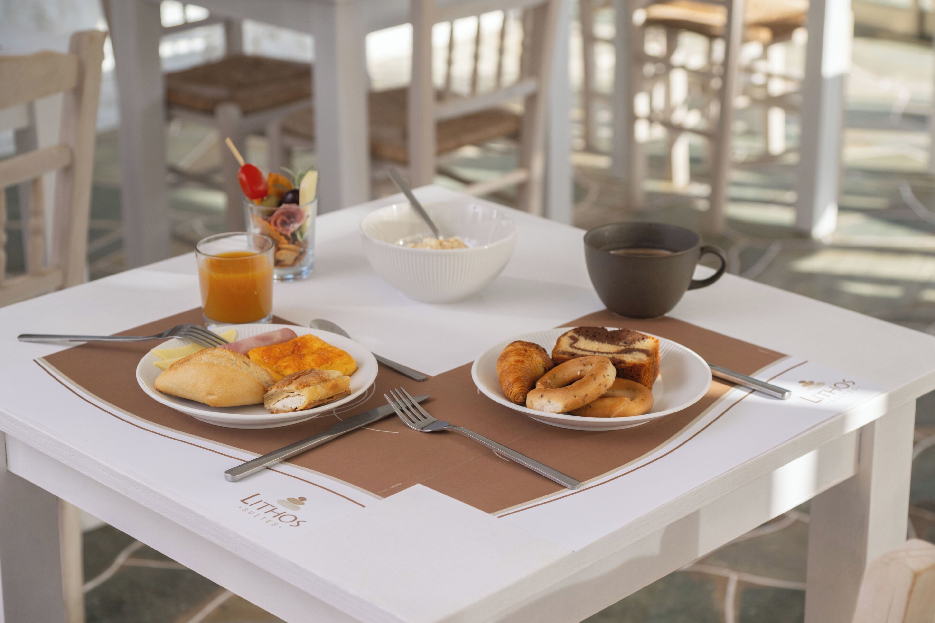 A dining table with plates of food, a glass of orange juice, a bowl, and a cup.