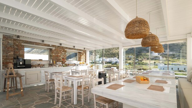 A spacious dining area with stone flooring, white furniture, and large windows offering a view of the mountains.