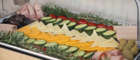A food display with various cheeses, cured meats, and vegetables.