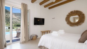 A bedroom with a bed, a television, a mirror, and a view of a pool and mountains.