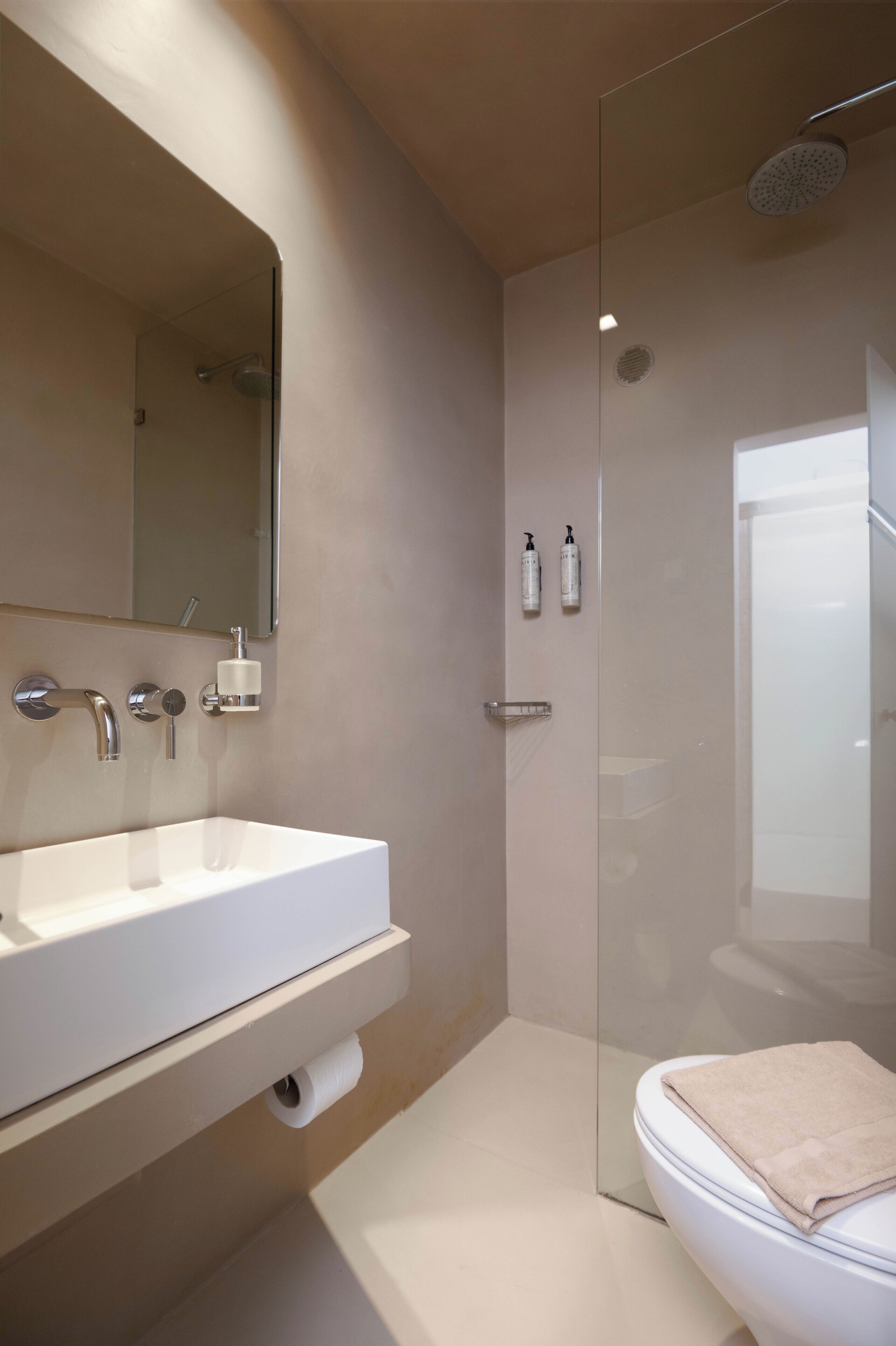 Een moderne badkamer met een witte wastafel, spiegel, douchecabine met glazen wanden en een toilet met een handdoek.