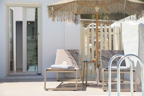 A sunlit outdoor seating area with a wooden chair, a small table, and a decorative umbrella. - Lithos Suites (Sifnos)
