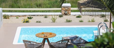 A pool area with wicker chairs, a table, and a stone structure.