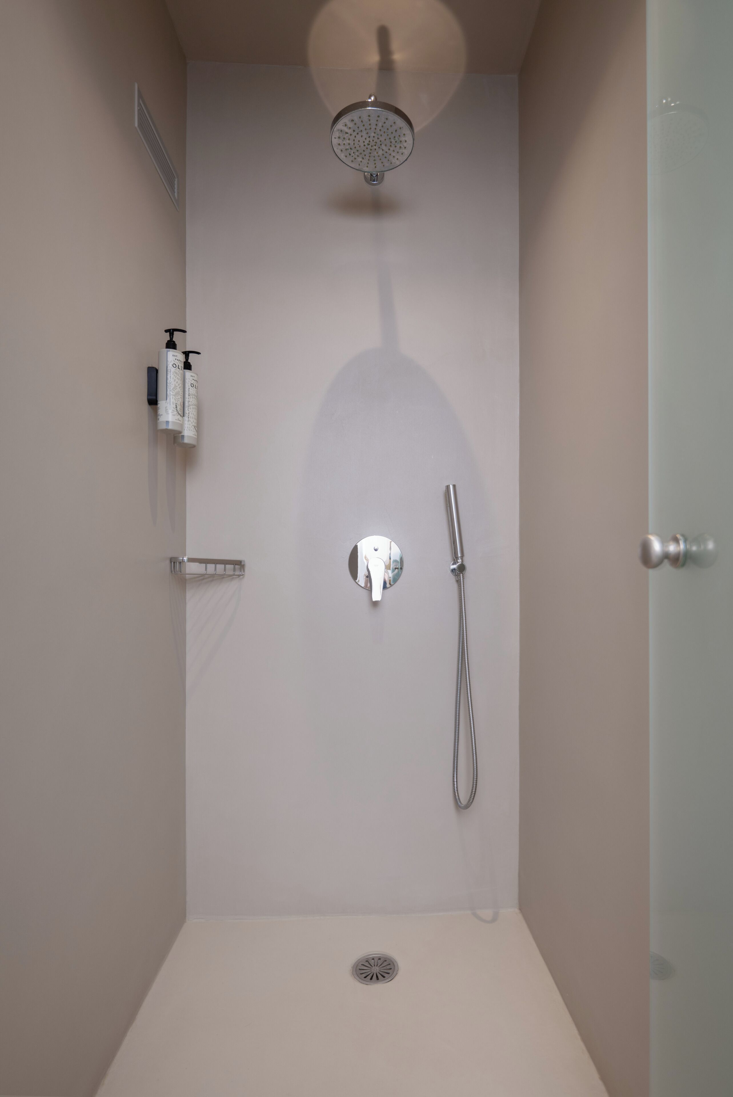 A shower with a handheld showerhead, a wall-mounted faucet, and a small shelf with toiletries.