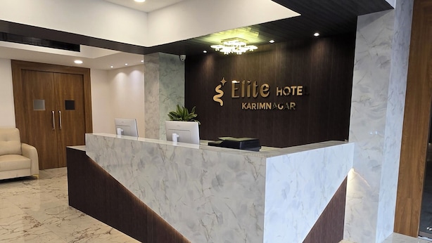 A hotel reception area with a marble reception desk, a wooden door, and a seating area with a sofa. - Elite Hotel Karimnagar (Karimnagar)