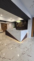 A hotel reception area with a marble reception desk, a wooden door, and a seating area with a sofa.