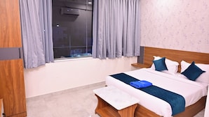 A hotel room with a bed, a wooden wardrobe, a window with curtains, and a wall with a floral pattern. - Elite Hotel Karimnagar (Karimnagar)