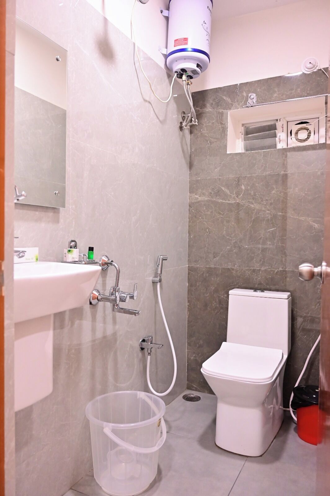 A modern bathroom with a white sink, two showerheads, a toilet, and a water heater mounted on the wall.