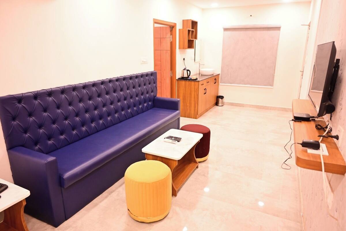 A modern living room with a blue sofa, a small wooden table, a yellow ottoman, a TV, and a wooden cabinet with a mirror.