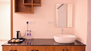A modern bathroom with a wooden vanity, a white sink, and a mirror above it. There are two bottles of water on the vanity and a kettle on the countertop. - Elite Hotel Karimnagar (Karimnagar)