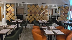 A modern restaurant with high ceilings, recessed lighting, and a patterned wall divider. Tables are set with menus and chairs are upholstered in green and orange. - Elite Hotel Karimnagar (Karimnagar)