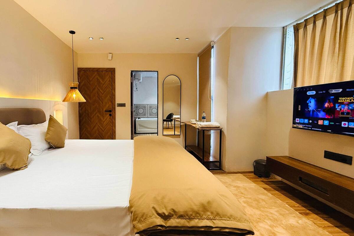 A hotel room with a large bed, a TV, a desk, and a bathroom visible through an open door.