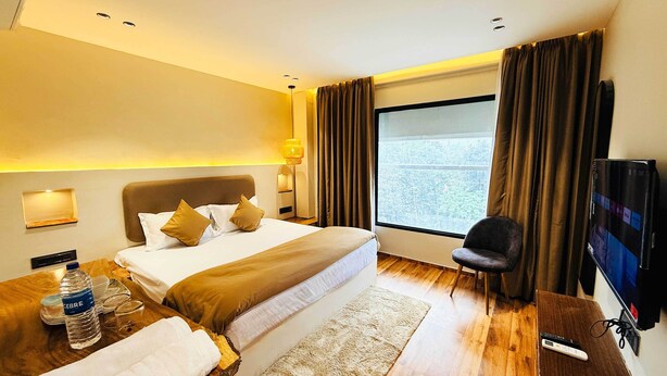 A hotel room with a bed, bedside tables, a TV, a chair, and a window with curtains. - HOTEL COCODAN (Indore)