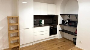 Una cocina moderna con armarios blancos, un estante escalonado de madera, una encimera negra y un microondas.