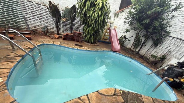 Una piscina con borde de piedra, rodeada por un muro de ladrillo y plantas en macetas.