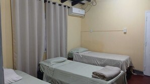 Una habitación con dos camas, una ventana con cortinas, un aire acondicionado y un enchufe en la pared.