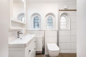 Ein modernes Badezimmer mit einem weißen Waschbecken, einer Toilette und drei Bogenfenstern.