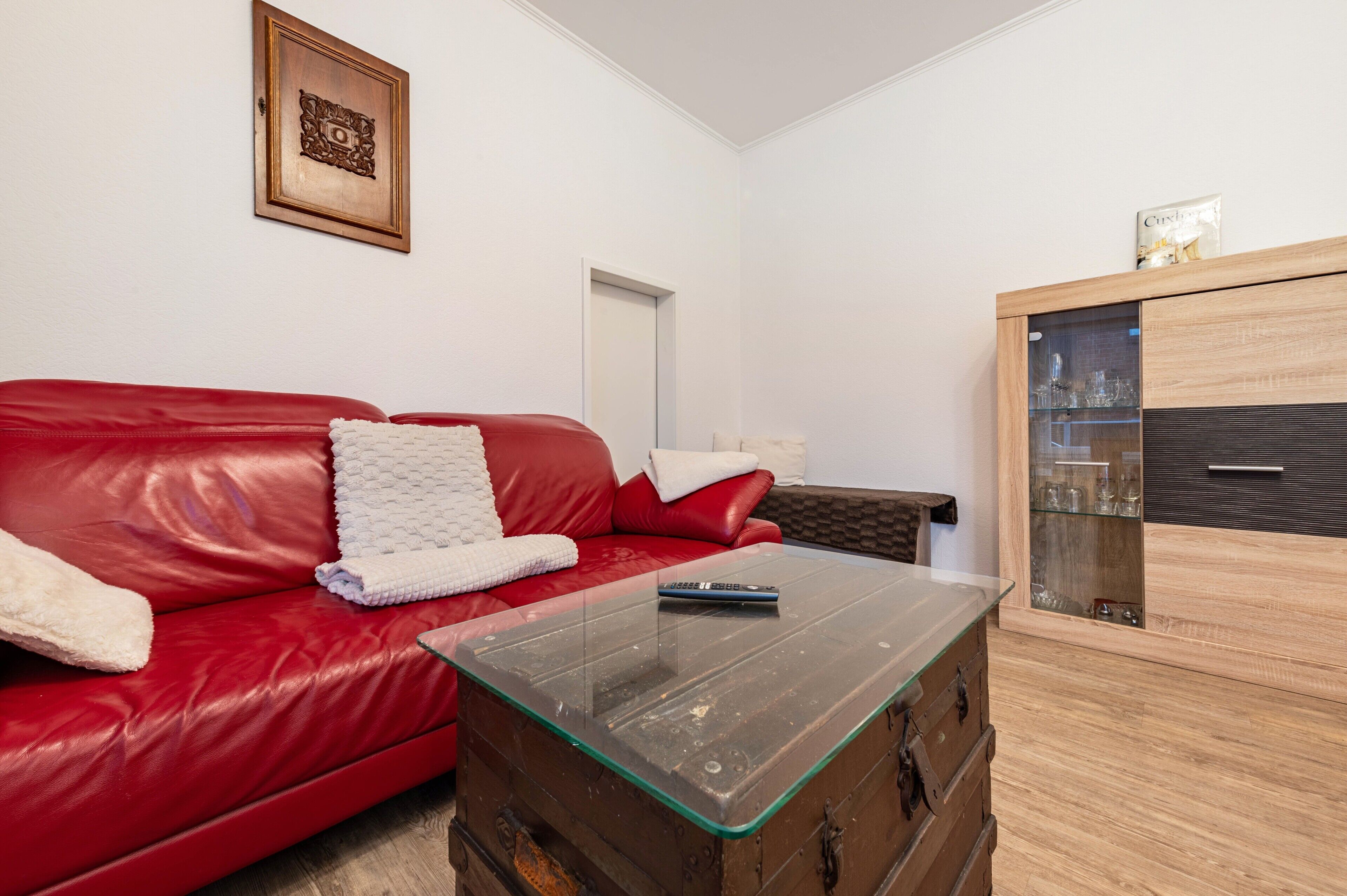 A red leather sofa with a glass coffee table and a wooden cabinet with glass doors.