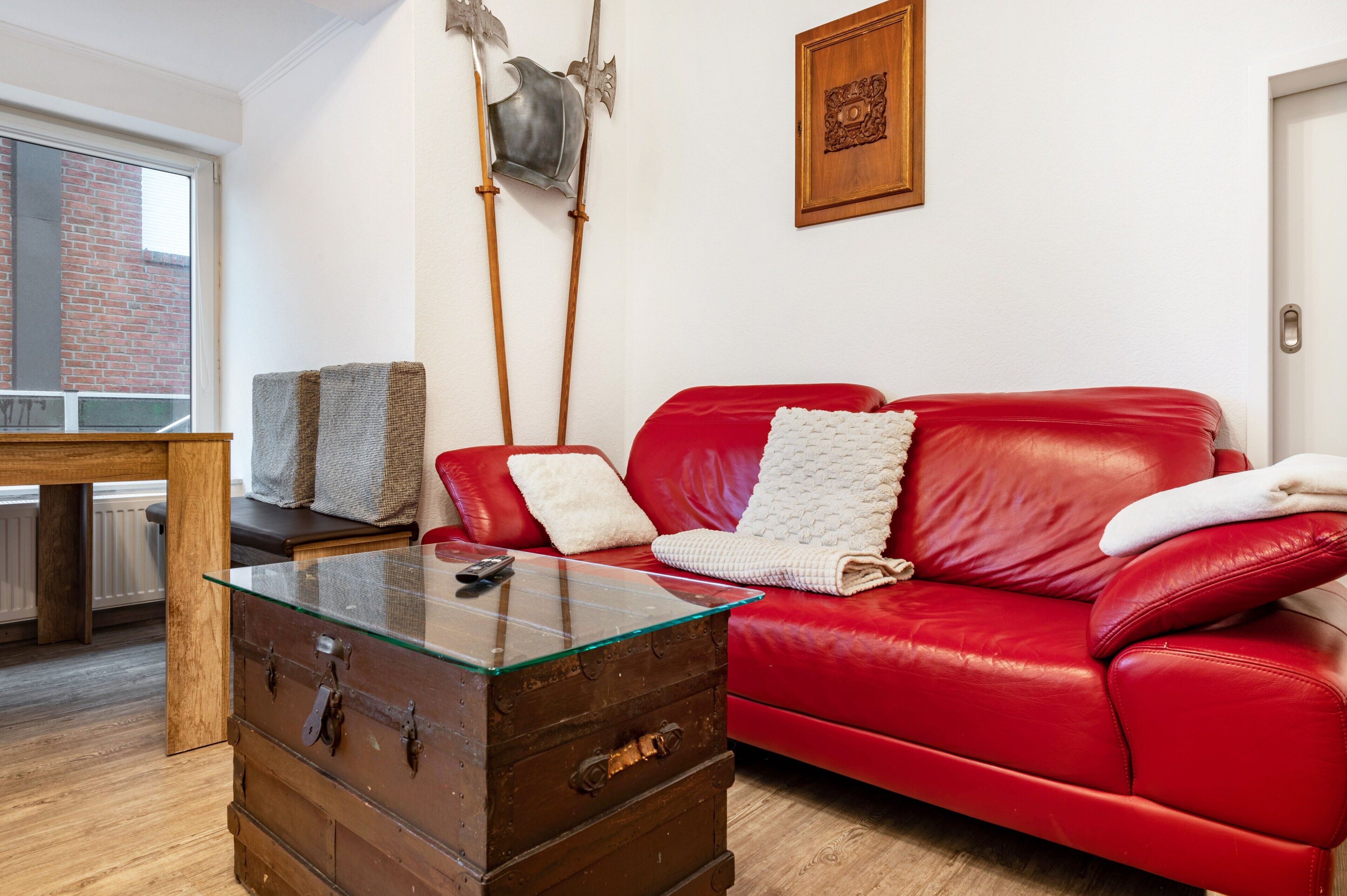 Un canapé en cuir rouge, une table basse en verre et une commode en bois.