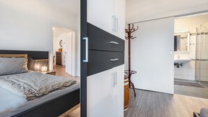 A modern bedroom with a bed, a wardrobe, and a bathroom visible through an open door.