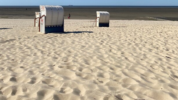 A beach with two white, fabric-covered structures, possibly storage or seating, on the sand.