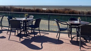 An outdoor seating area with tables and chairs, overlooking a beach and ocean.