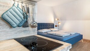 Ein modernes Zimmer mit einem Bett, einem fest eingebauten Herd und Küchenutensilien, die an der Wand hängen.