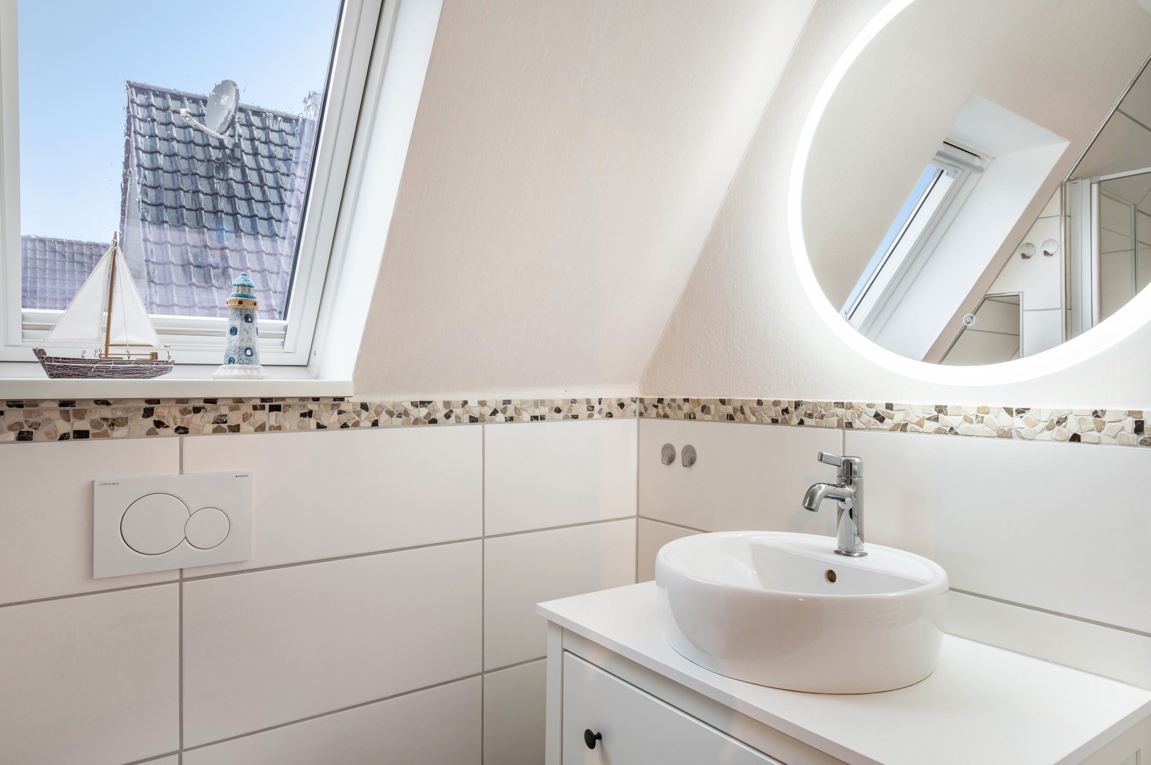 A modern bathroom with a skylight, a round mirror, a white sink, and a small ship decoration.
