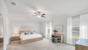 A bedroom with a bed, bedside tables, a desk, a ceiling fan, and a window with curtains. - Modern 4BR/2BA Home Near Airport, London HS & Local Businesses<br>Welcome to this newly built, professionally designed 4-bedroom, 2-bath home in Corpus Christi—perfect for business travelers, families, and groups of up to 8 guests. Enjoy a bright ope (Corpus Christi)