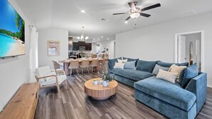 A modern living room with a blue sofa, wooden coffee table, and a dining area with a kitchen in the background. - Modern 4BR/2BA Home Near Airport, London HS & Local Businesses<br>Welcome to this newly built, professionally designed 4-bedroom, 2-bath home in Corpus Christi—perfect for business travelers, families, and groups of up to 8 guests. Enjoy a bright ope (Corpus Christi)