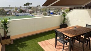 A patio with a table and chairs, a small garden area with artificial grass, and a view of a sports field. - Duplex with private terrace and parking 15 minutes from Seville (Dos Hermanas)
