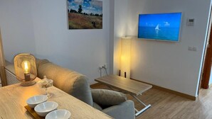 A modern living room with a sofa, a coffee table with bowls, a wall-mounted TV, and a painting. - Duplex with private terrace and parking 15 minutes from Seville (Dos Hermanas)