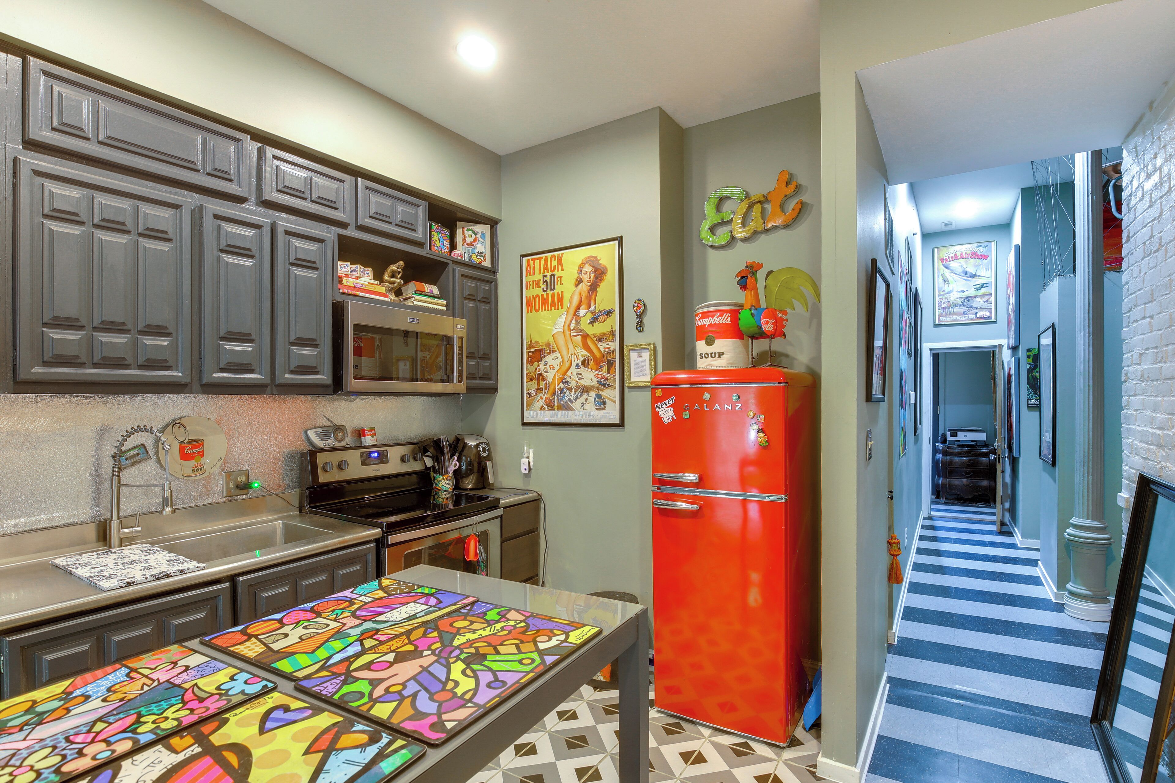 A kitchen with gray cabinets, a red refrigerator, and a colorful table.