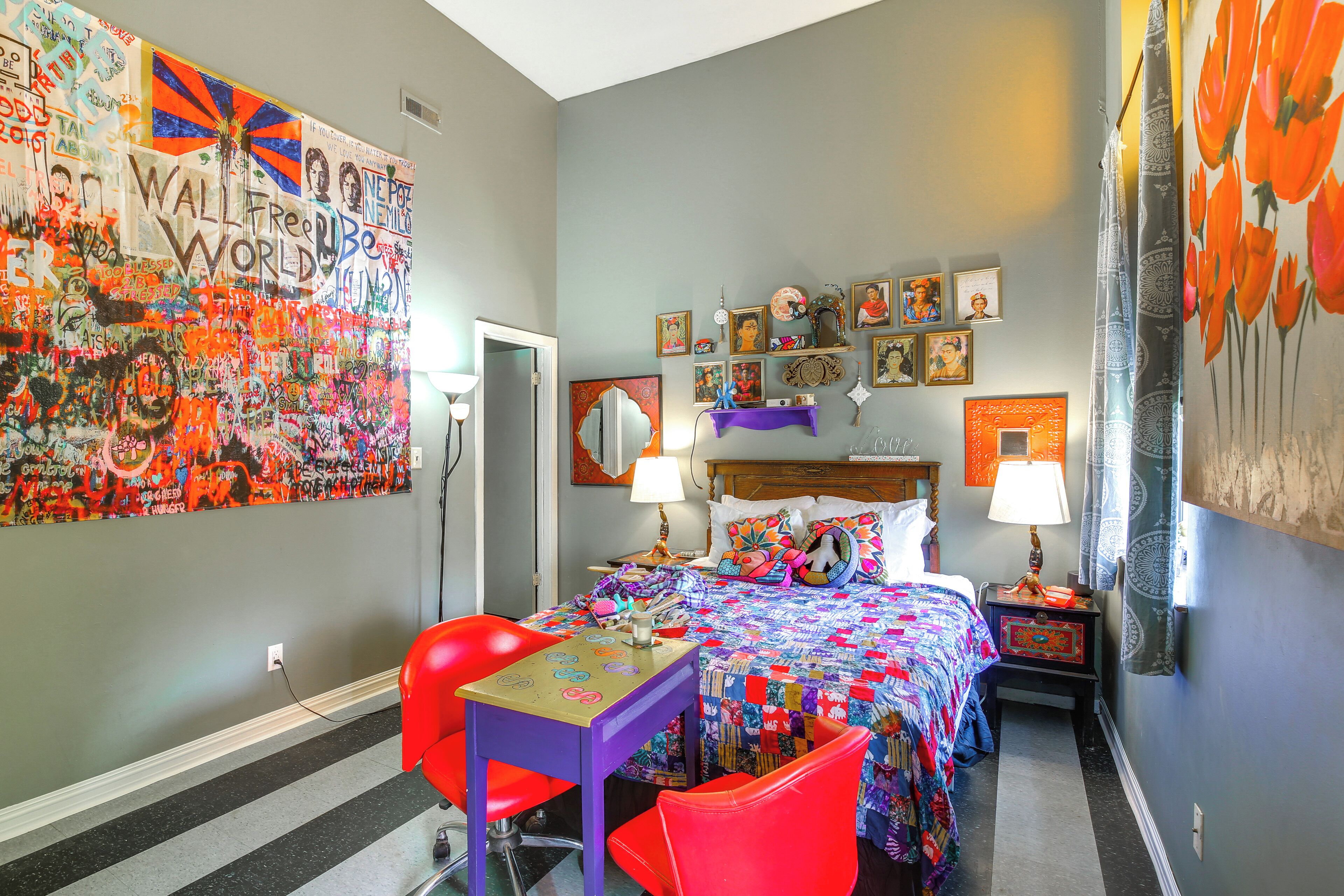 Une pièce comprenant un lit, un bureau et une chaise. Un mur est décoré de différents objets, et il y a une porte.