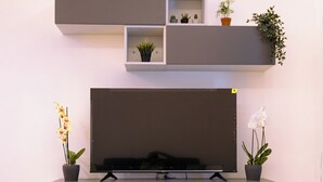 Een moderne woonkamer met een flatscreen televisie, twee potorkideeën en een minimalistische wandplank.