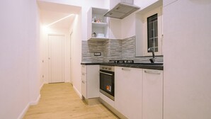 Een smalle keuken met witte kasten, een zwart aanrecht en een betegelde spatwand.