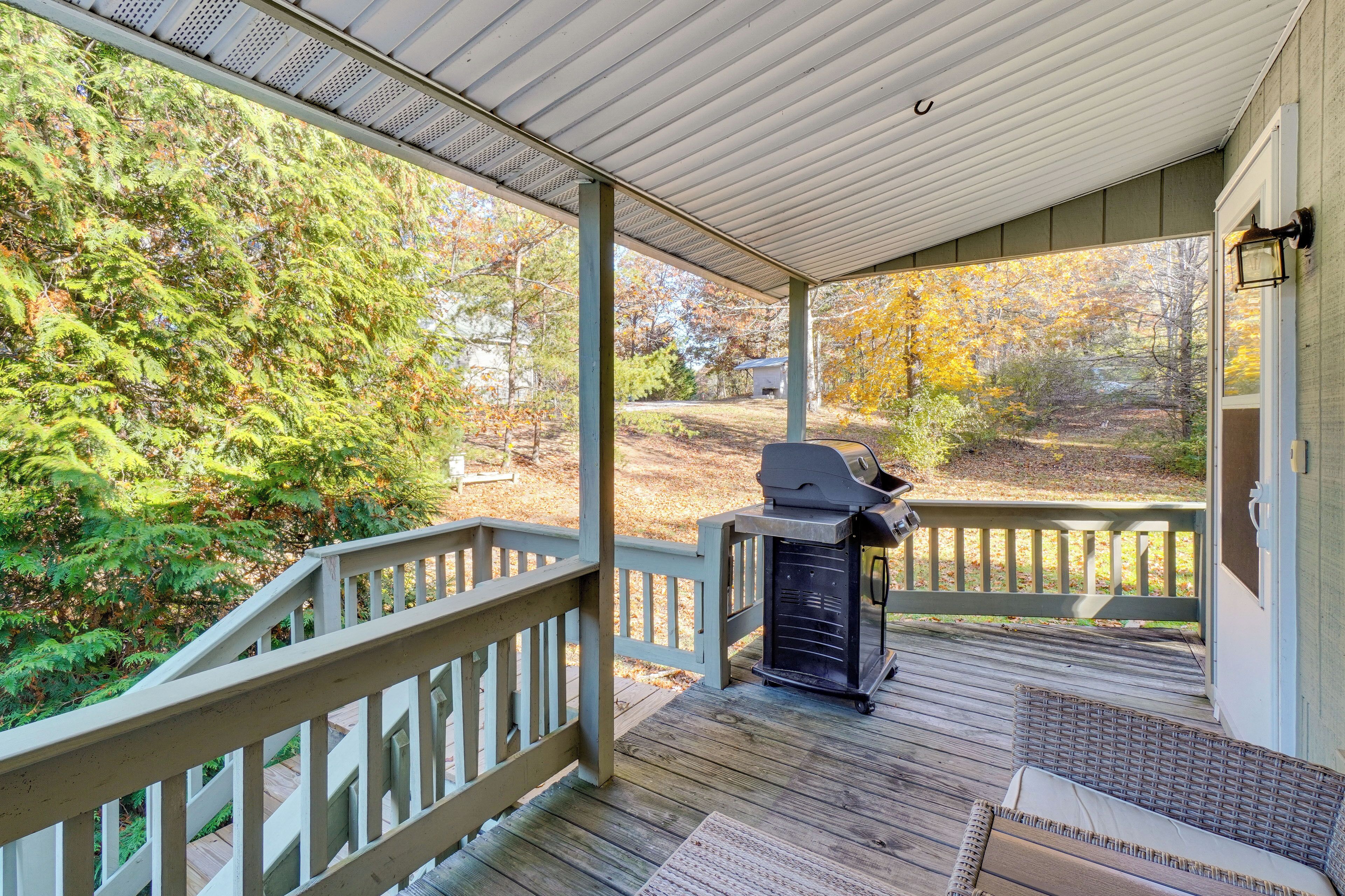 A covered porch with a grill, wooden deck, and a view of a forested area.