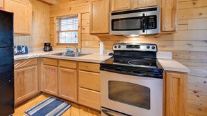 A wooden-paneled kitchen with a microwave, stove, and sink. - Cabin Along Rough River! Views, Fire Pit & Grill (Falls of Rough)