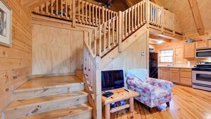 A wooden cabin interior with a wooden staircase, a sofa, a television, and a kitchen area. - Cabin Along Rough River! Views, Fire Pit & Grill (Falls of Rough)