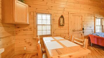 A wooden cabin interior with a dining table, chairs, a cabinet, and a bed.